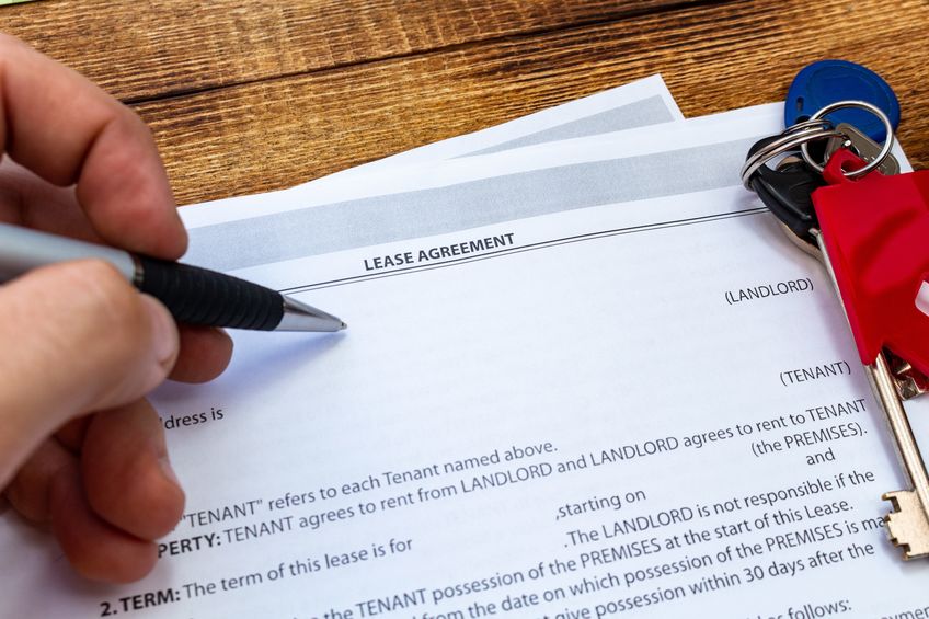 Close-up on a person's hand holding a pen to a document labeled "lease agreement" at the top